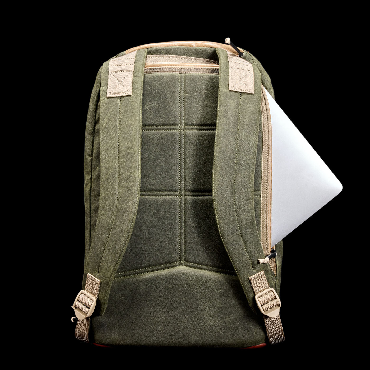 A green backpack with tan straps, holding a silver laptop in a side zipper pocket, on a black background.