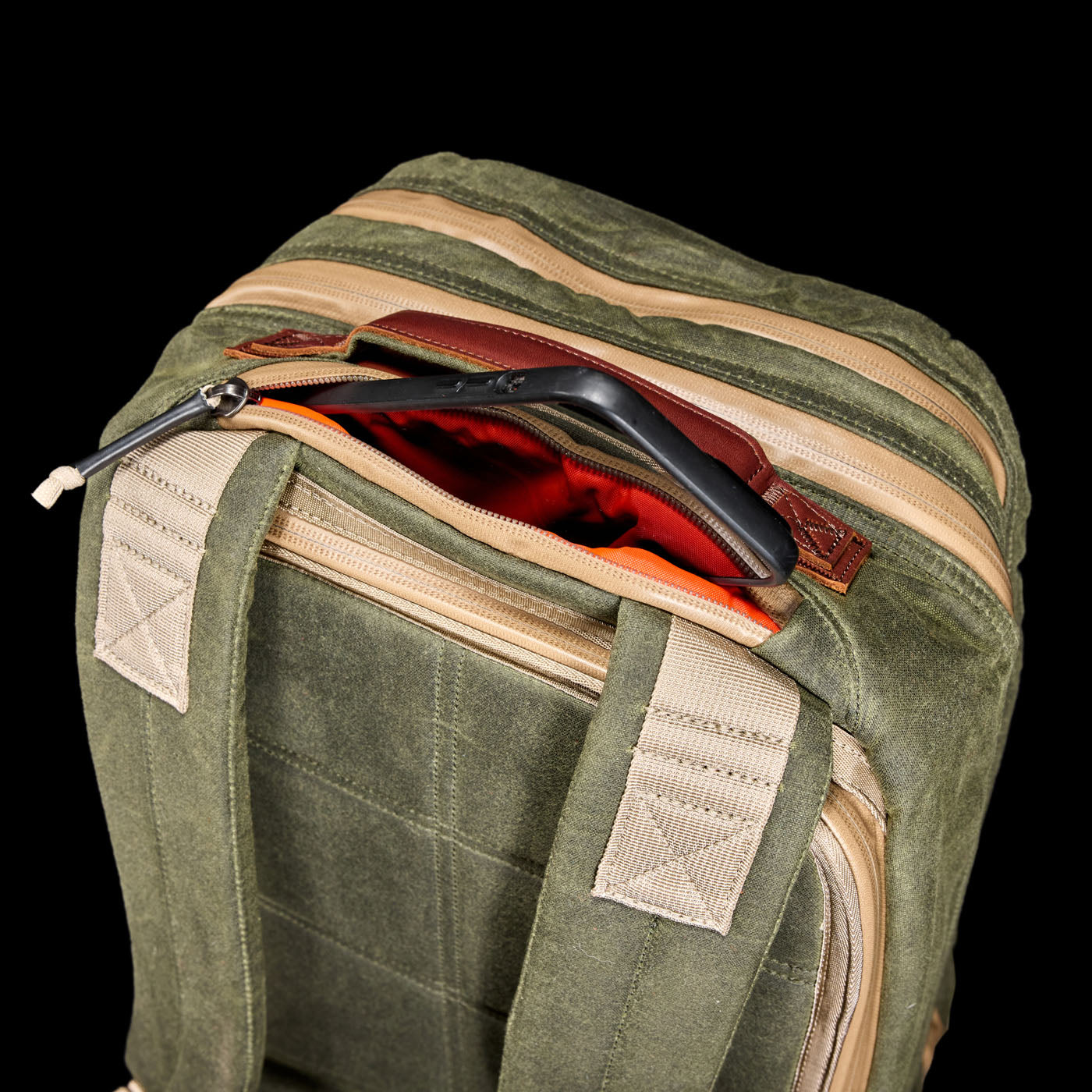 Green backpack with tan straps and an open zipper pocket revealing a phone inside against a black background.