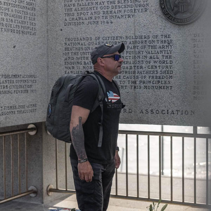 Man in GORUCK gear with rucksack at memorial wall, honoring military service