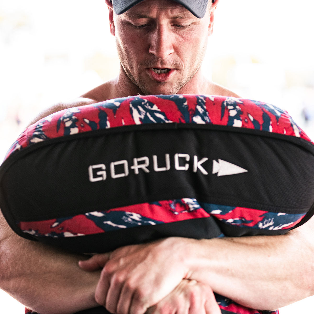 Man holding a red and blue GORUCK sandbag tightly to his chest while working out.