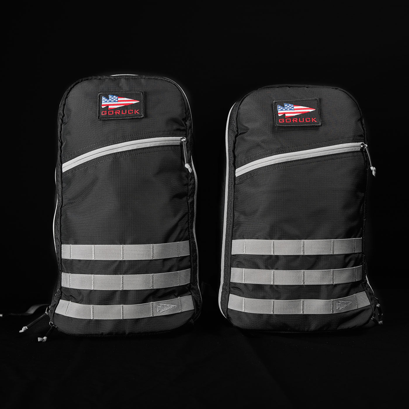 Two black backpacks with gray horizontal stripes and a GORUCK American flag patch, on a black background.