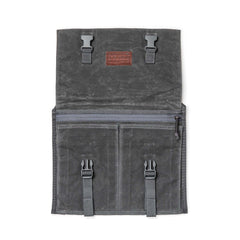 The Waxed Canvas Claymore Sling Bag, featuring buckles, zippers, and a leather patch, is displayed flat on a white background.