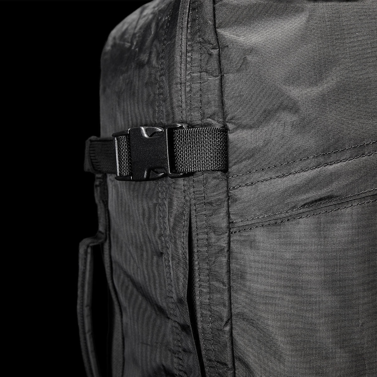 Close-up of a black backpack with a plastic buckle and visible stitching against a dark background.