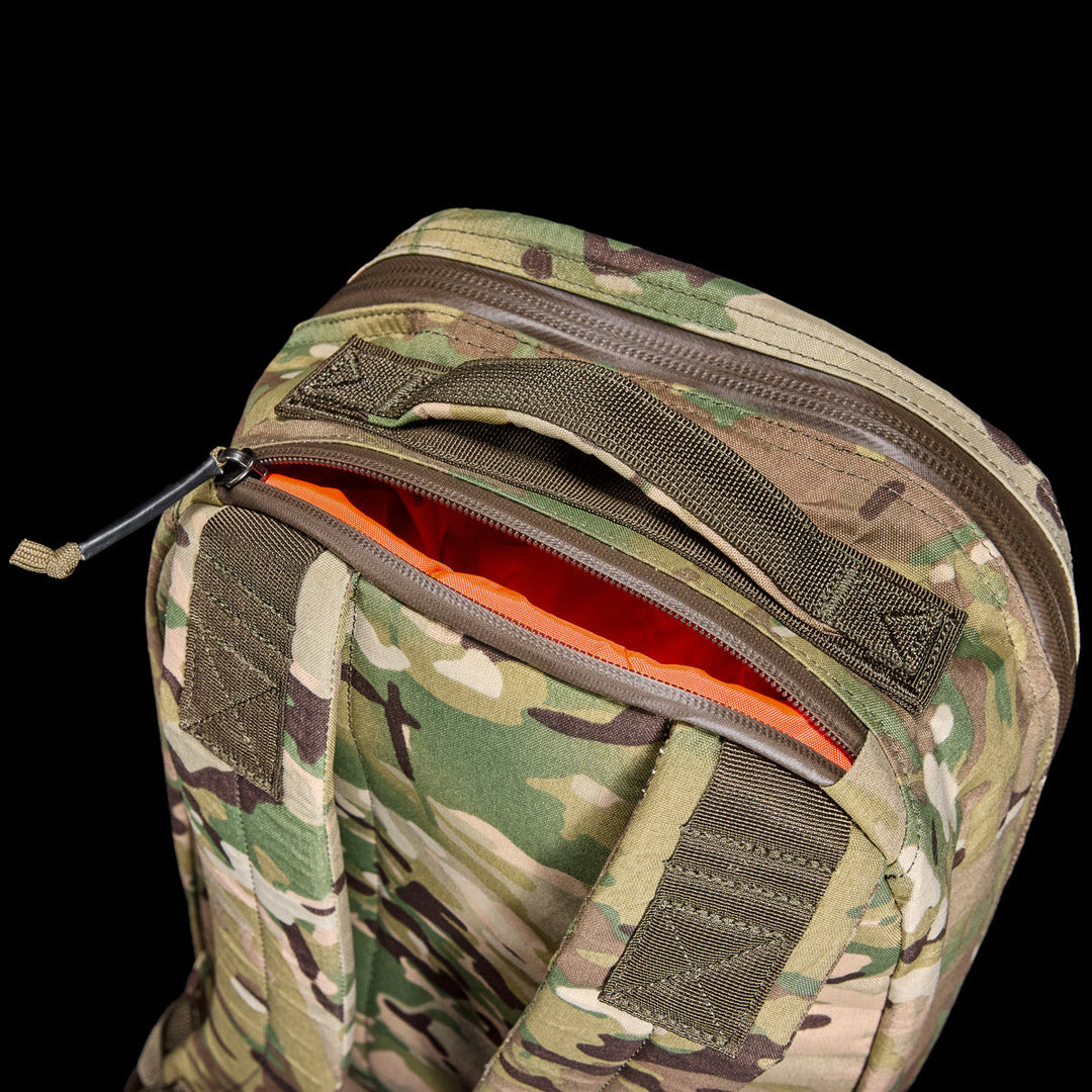 The GORUCK Bullet X-PAC daypack features a camouflage exterior with a partially unzipped top, revealing its bright orange weatherproof X-PAC interior.
