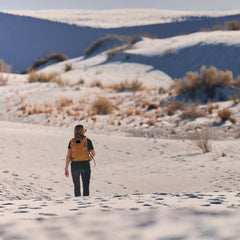Person rucking with a GORUCK backpack in a sandy desert landscape with sparse vegetation
