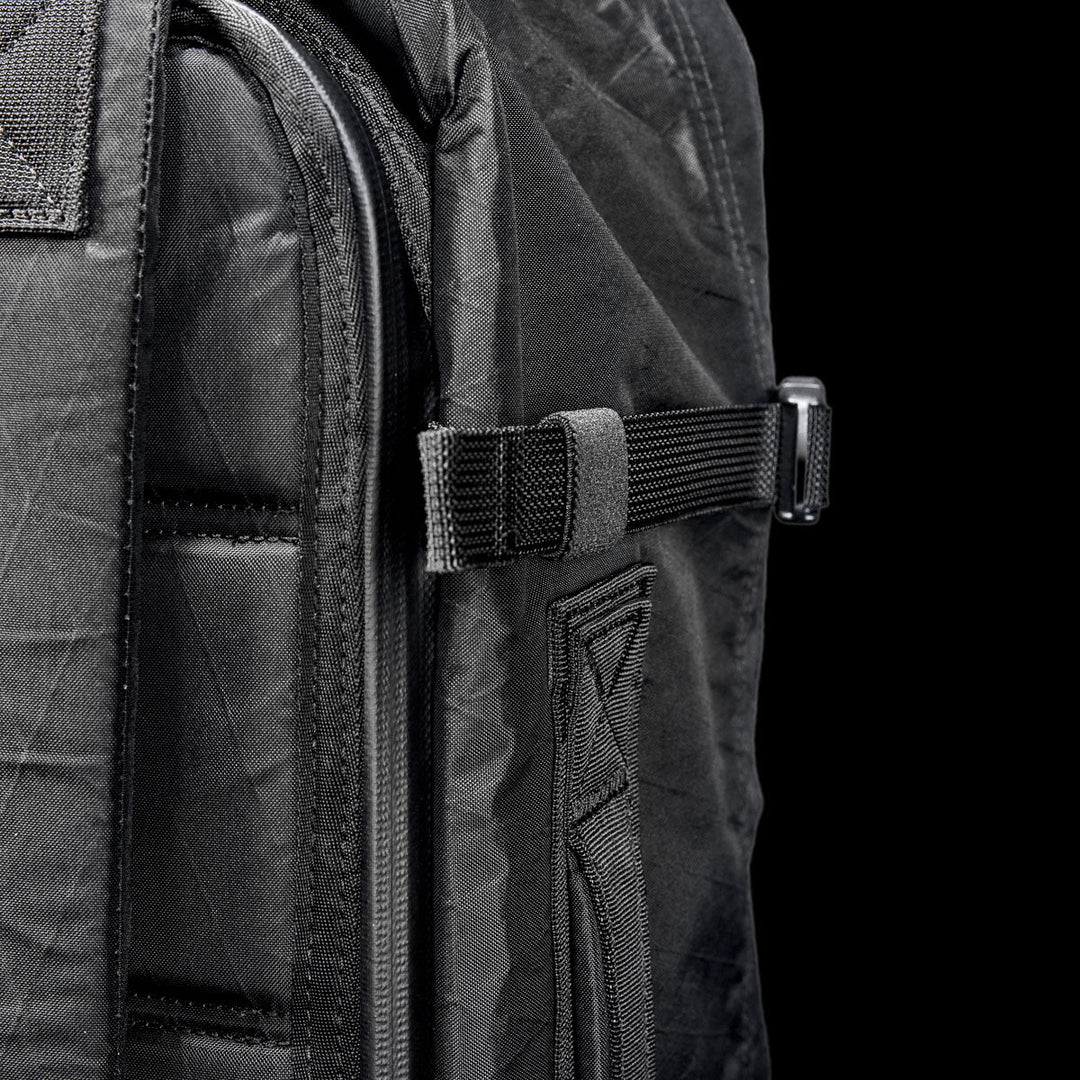 Close-up of the GORUCK GR3 - X-PAC backpack, crafted from waterproof material with a side strap and buckle, set against a plain black background.