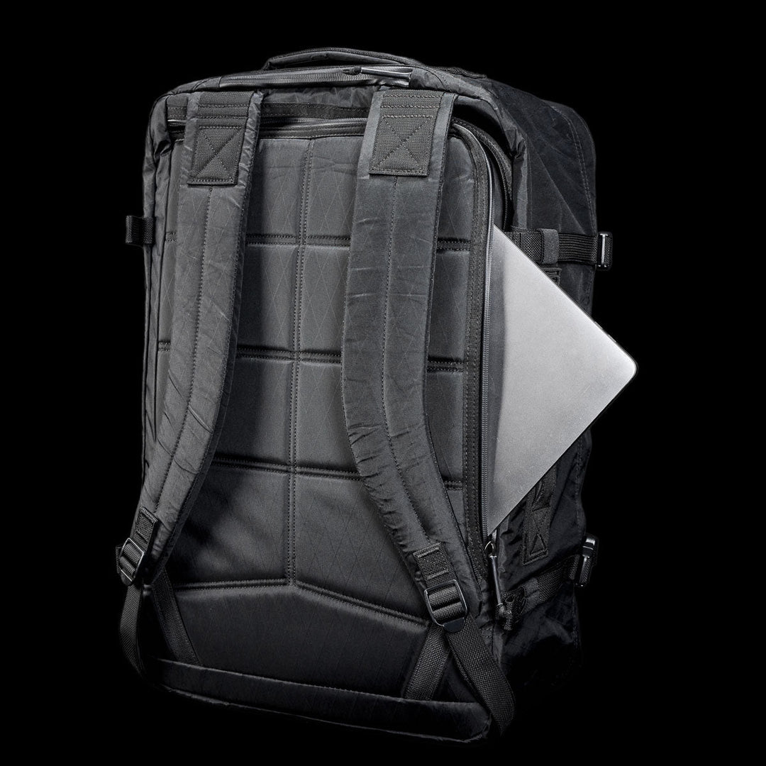 A black GORUCK GR3 - X-PAC backpack with padded straps, made from waterproof material, holds a silver laptop partially in its back compartment.