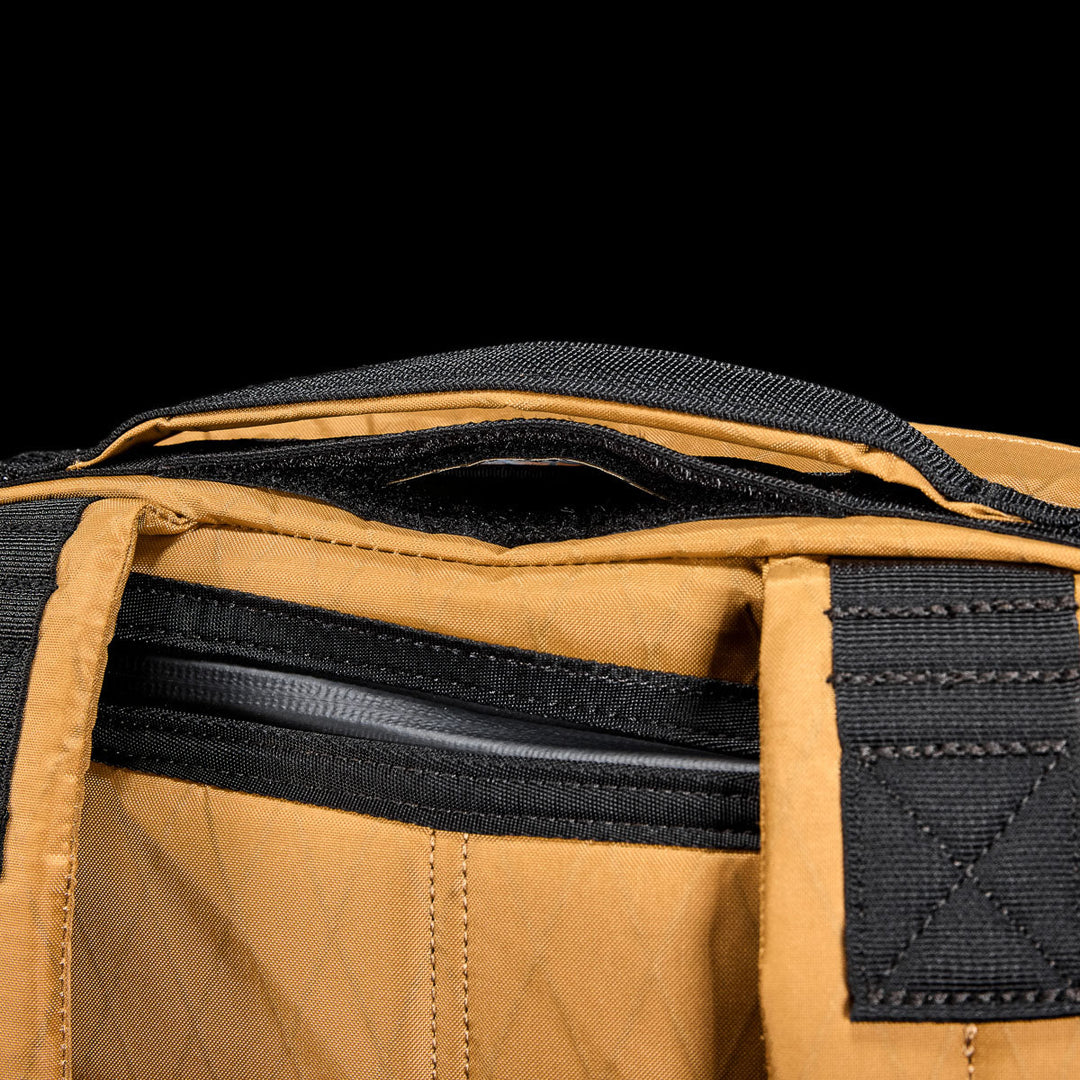 Close-up of the GORUCK GR0 - X-PAC bag in brown, showing black zipper, handle, and fabric accents, with visible stitching. Lightweight and waterproof X-PAC construction.