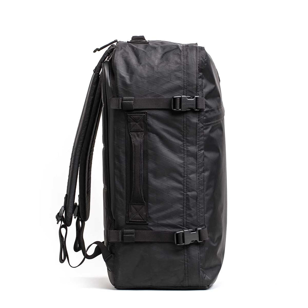 The GORUCK GR3 - X-PAC is a black waterproof duffel with backpack straps and a side handle, shown standing upright on a white background—ideal for use as carry-on luggage.