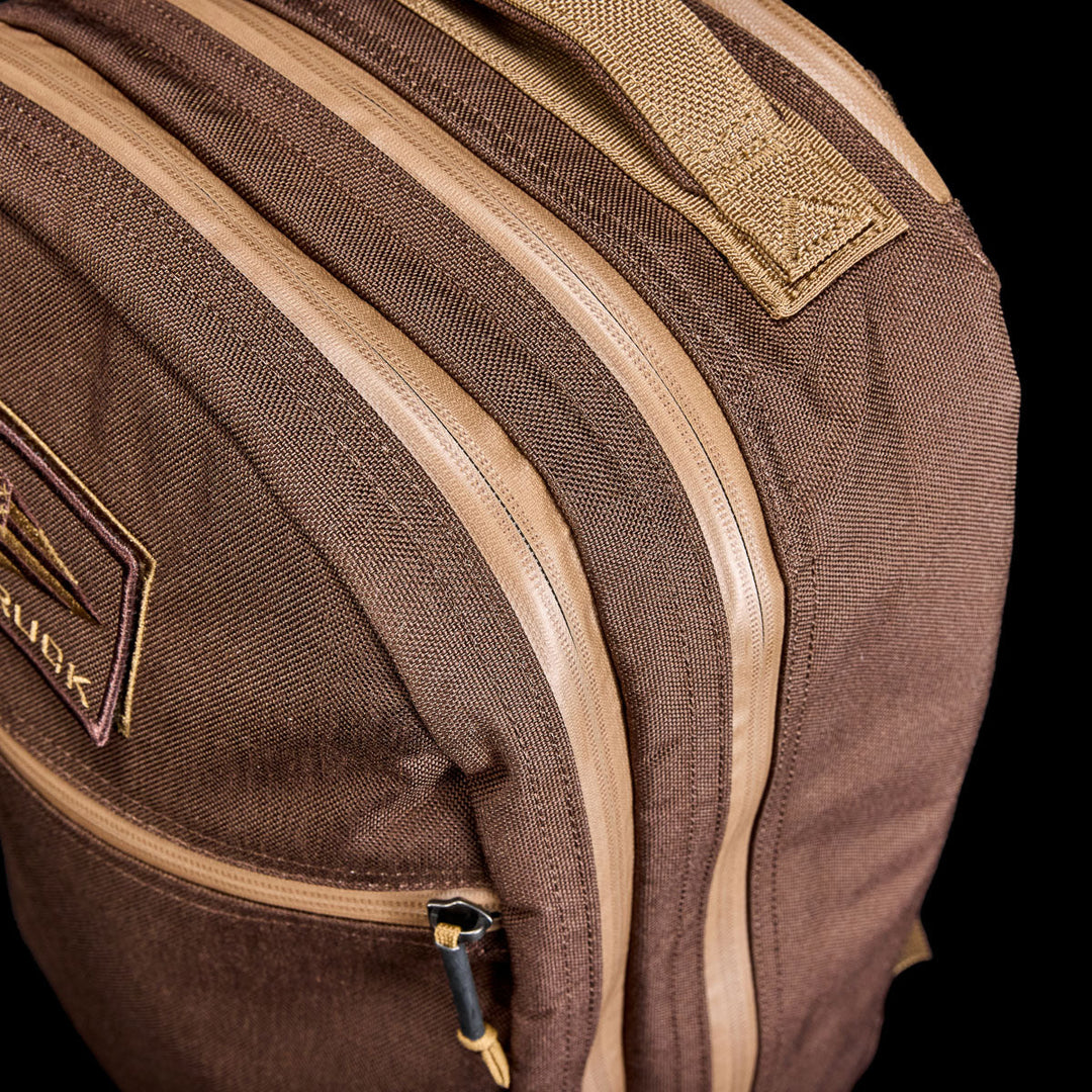 Close-up of the Bullet Ruck - Ballistic Nylon Cordura - 18L backpack, featuring tan zippers, a stitched handle, and a bombproof laptop compartment, set against a black background.