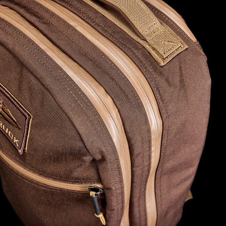 Close-up of the Bullet Ruck - Ballistic Nylon Cordura - 18L backpack, featuring tan zippers, a stitched handle, and a bombproof laptop compartment, set against a black background.