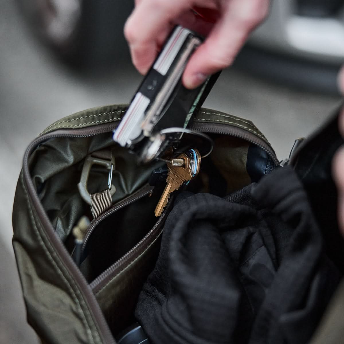 Hand placing keys and multitool into GORUCK rucksack with gear inside