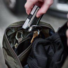 Hand placing keys and multitool into GORUCK rucksack with gear inside