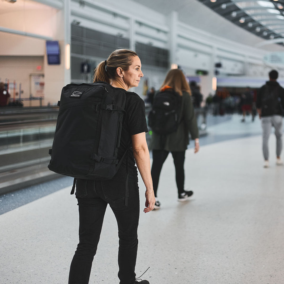 A traveler with a GORUCK GR3 - X-PAC ultra-waterproof backpack stands in a busy airport terminal, gazing at the crowd ahead.
