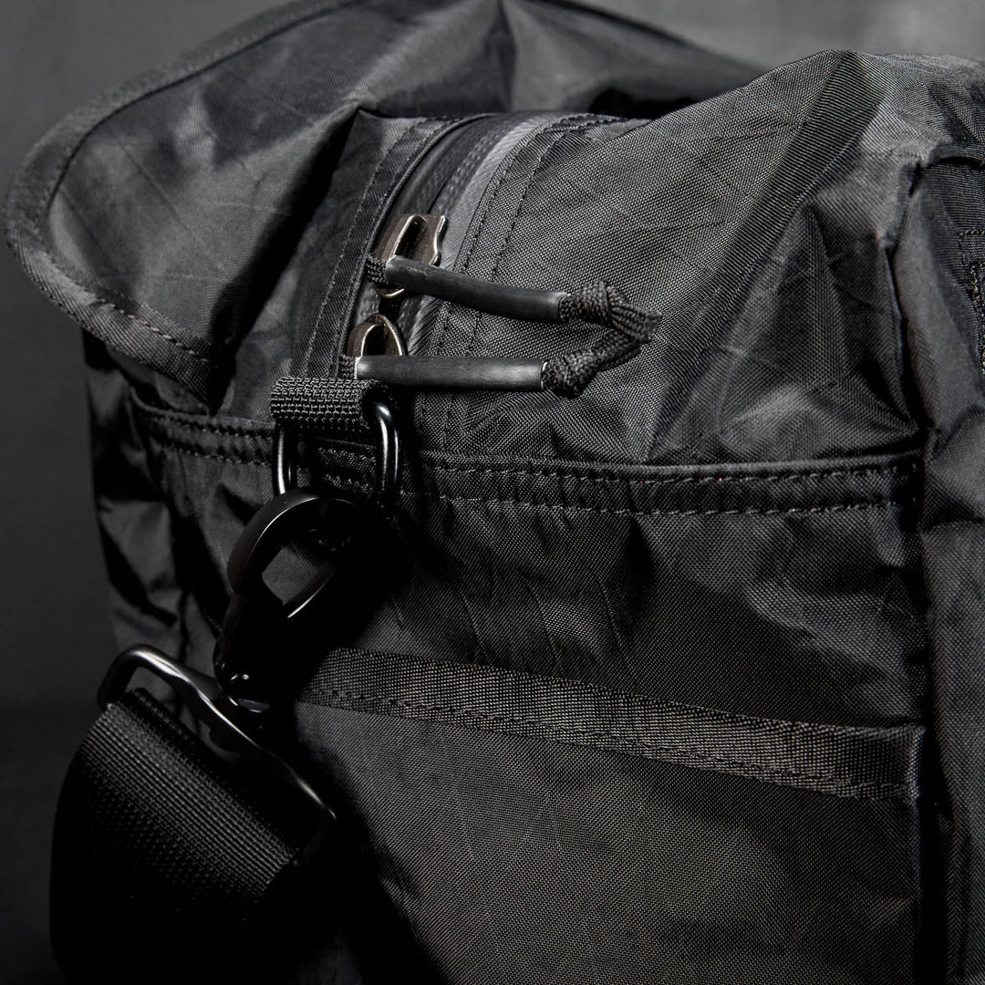 Close-up of the Kit Bag - X-PAC in black, crafted from X-PAC VX21 nylon with a zipper, strap, and metal clasp, set against a dark background.