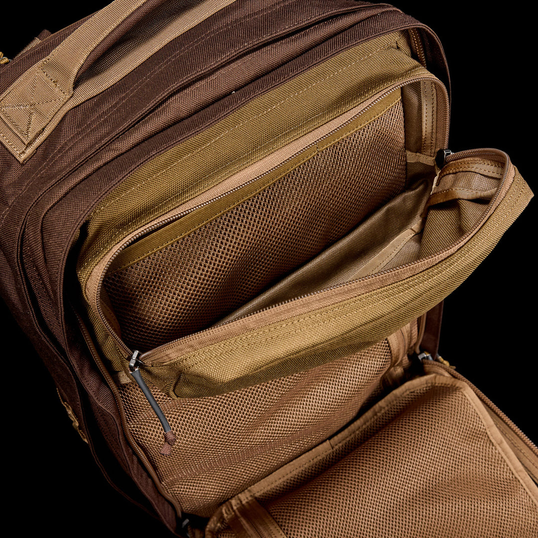 The GORUCK GR2 travel backpack in brown and tan features multiple zippered mesh pockets and compartments, and is designed to be carry-on compliant for your convenience.