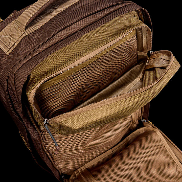The GORUCK GR2 travel backpack in brown and tan features multiple zippered mesh pockets and compartments, and is designed to be carry-on compliant for your convenience.