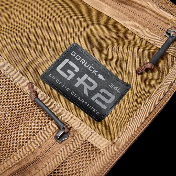 Close-up of GR2 by GORUCK—a tan travel backpack with mesh zippered pockets and a 34L patch, inspired by Special Forces rucks and designed to be carry-on compliant.