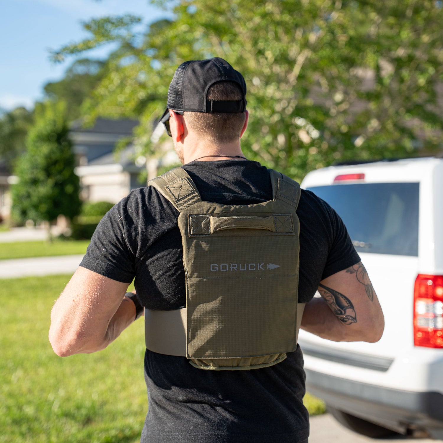 Man wearing a black cap and the Achilles Vest stands outside near a white vehicle on a sunny day.
