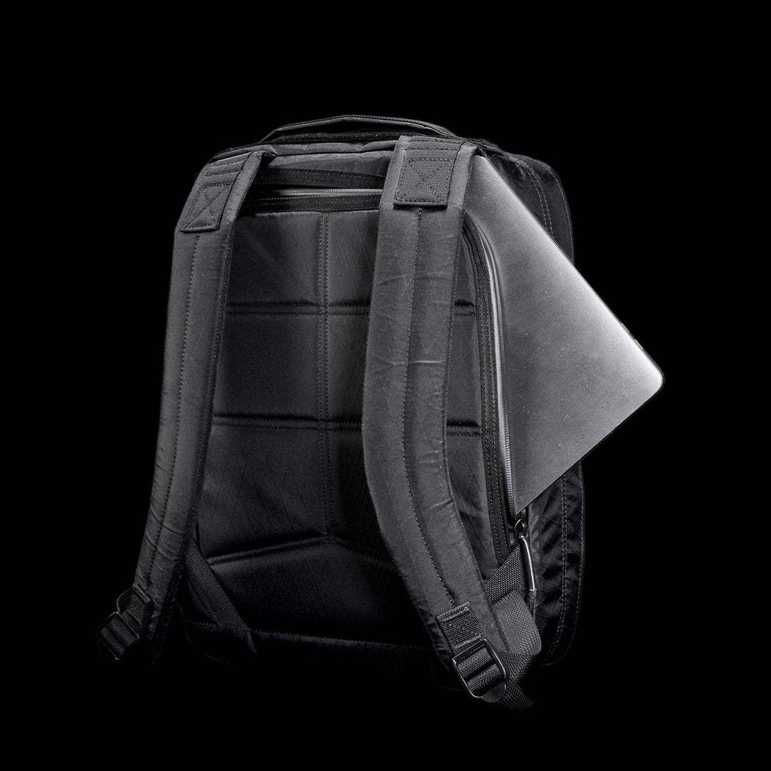 The GORUCK GR0 - X-PAC is a black backpack crafted from lightweight, waterproof X-PAC material with padded straps, shown holding a partially visible silver laptop against a black background.