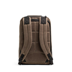 The back view of the GR1 USA - Heritage by GORUCK reveals a padded waxed canvas backpack in brown, featuring adjustable shoulder straps and subtle black accents.