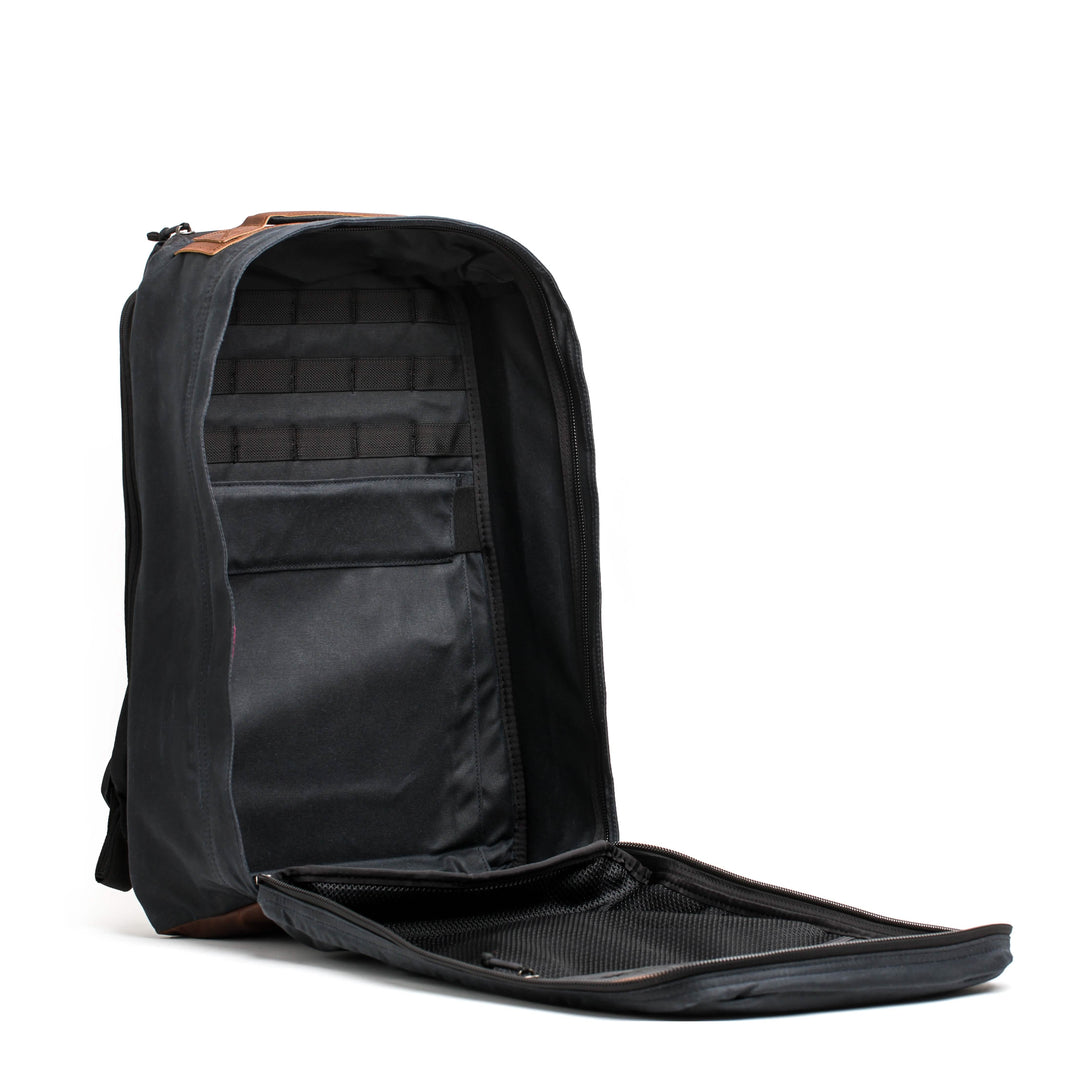 The GR1 USA - Heritage by GORUCK is a black heritage rucksack made from waxed duck canvas with a spacious interior and multiple compartments, designed to stand upright.