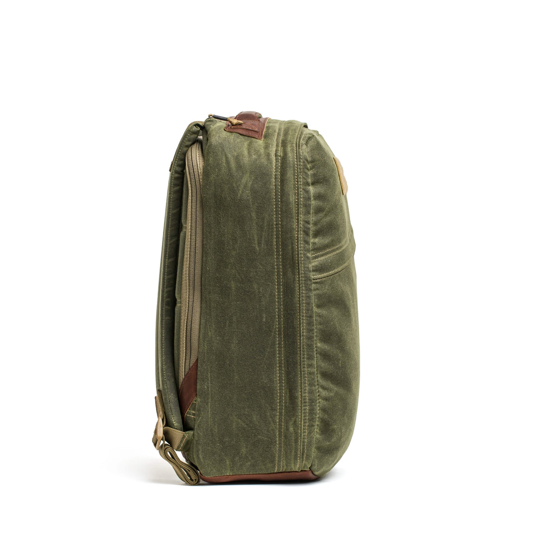 The side view of a GR1 USA - Heritage backpack by GORUCK features green waxed duck canvas, zippers, and leather accents against a white background, showcasing its classic heritage rucksack style.