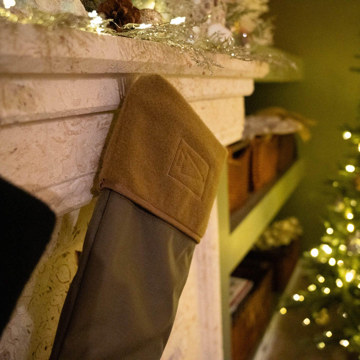 GORUCK tactical stocking hanging on a decorated mantel beside a lit Christmas tree