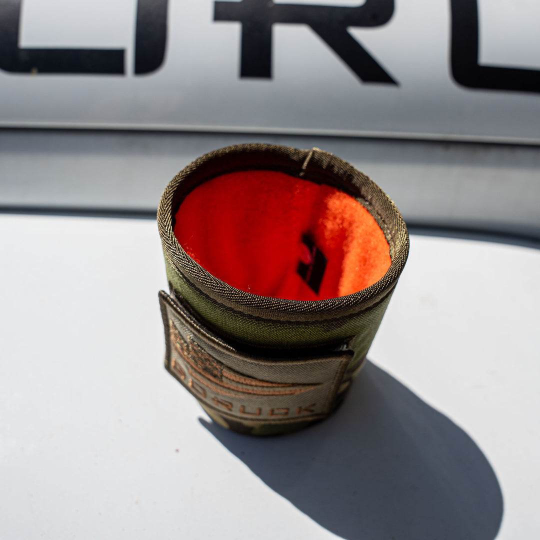 A khaki and orange GORUCK Ballistic Beer Jacket made from 1000D CORDURA rests on a white surface with black letters in the background.
