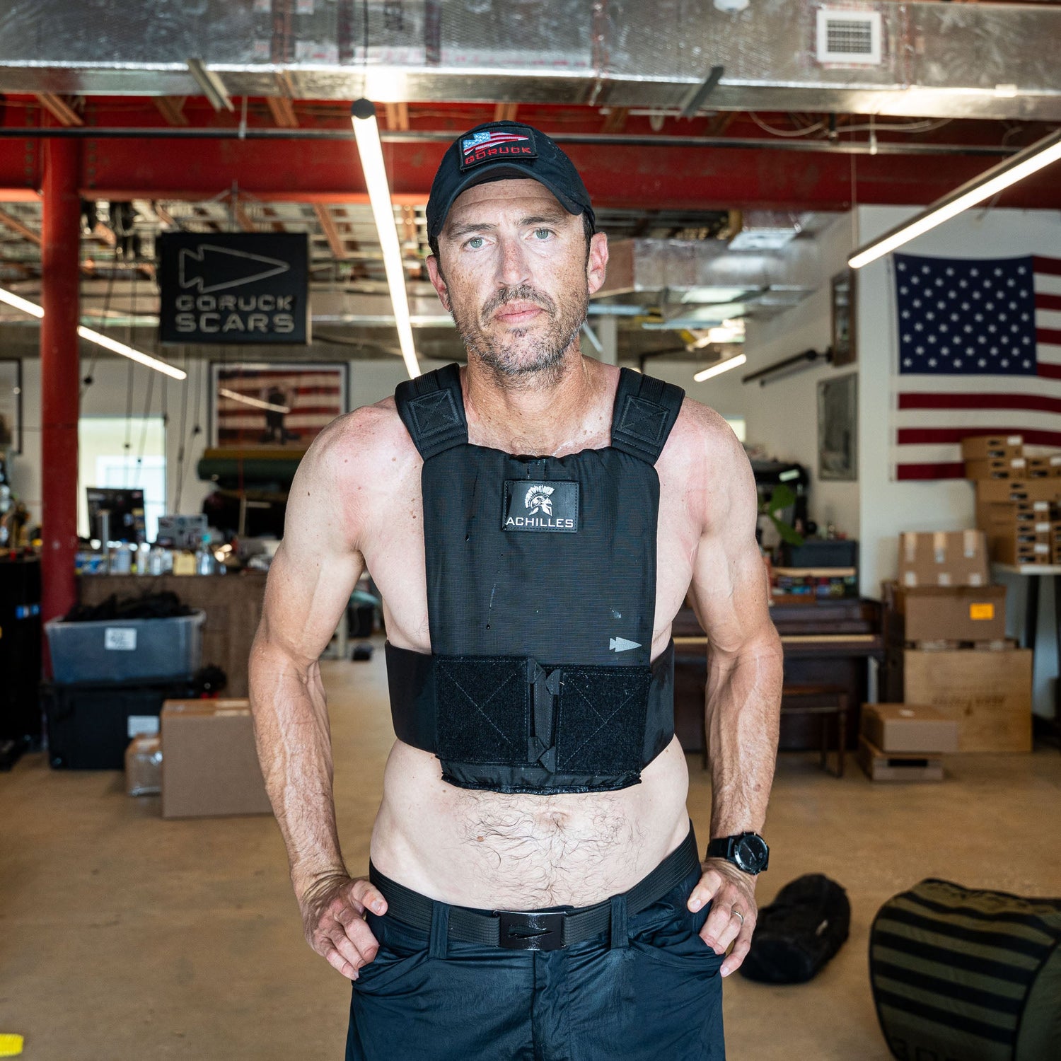 A man wears the Achilles | Men's Weighted Vest indoors with an American flag in the background.