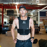 A man wears the Achilles | Men's Weighted Vest indoors with an American flag in the background.