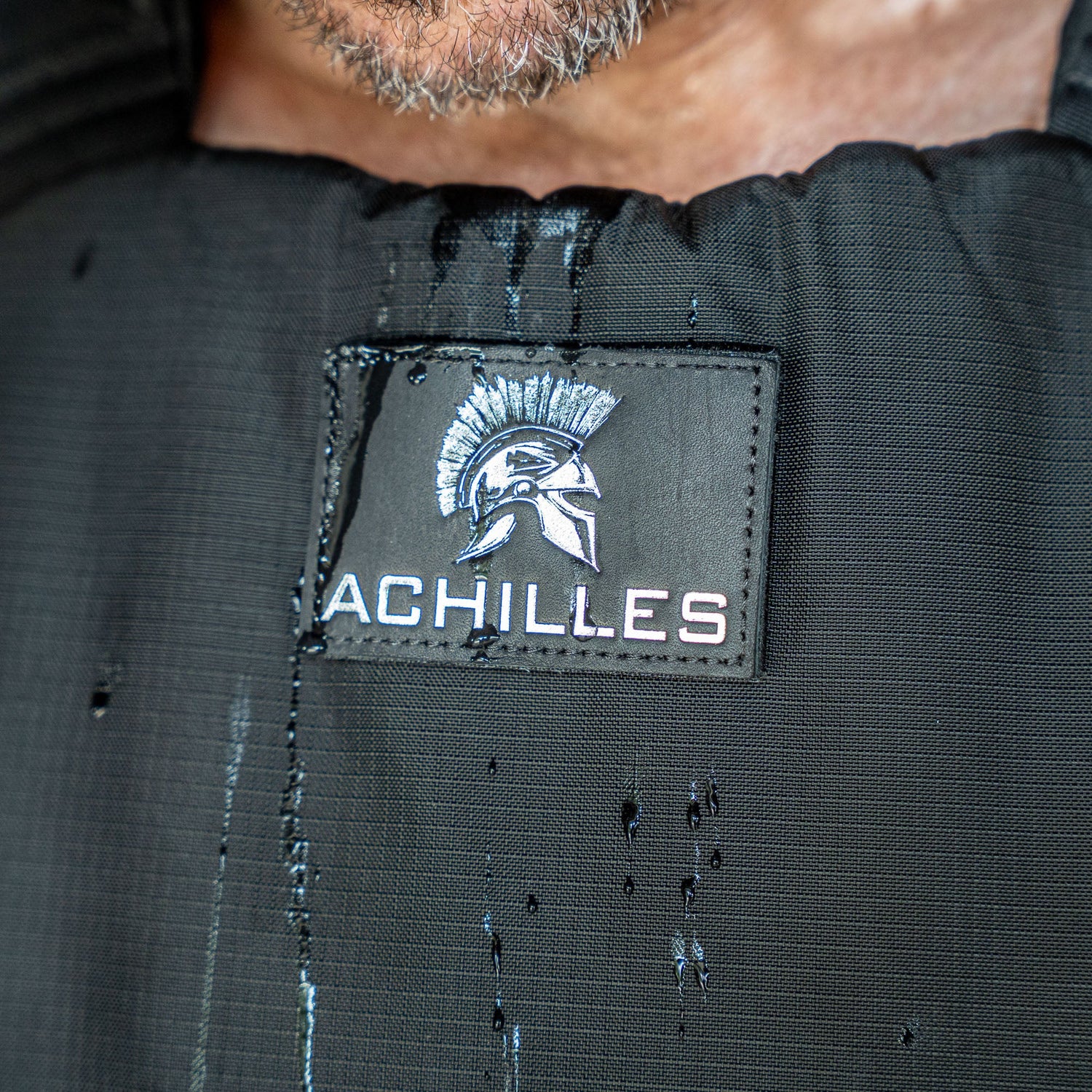 Close-up of the Achilles | Men's Weighted Vest featuring a Spartan helmet logo and water droplets on its premium exterior.