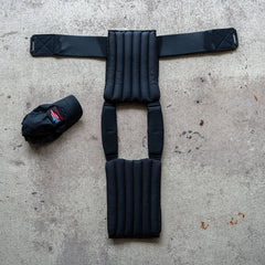 The Achilles | Men's Weighted Vest, featuring padded non-toxic construction, is laid flat on concrete beside a black baseball cap.