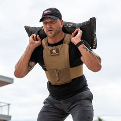 A man wearing the Achilles | Men's Weighted Vest lifts a 50lb sandbag on his shoulders during an outdoor workout.
