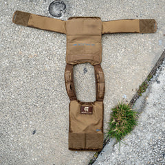 Two Achilles | Men's Weighted Vests in brown lay open on cracked concrete beside a small patch of grass.
