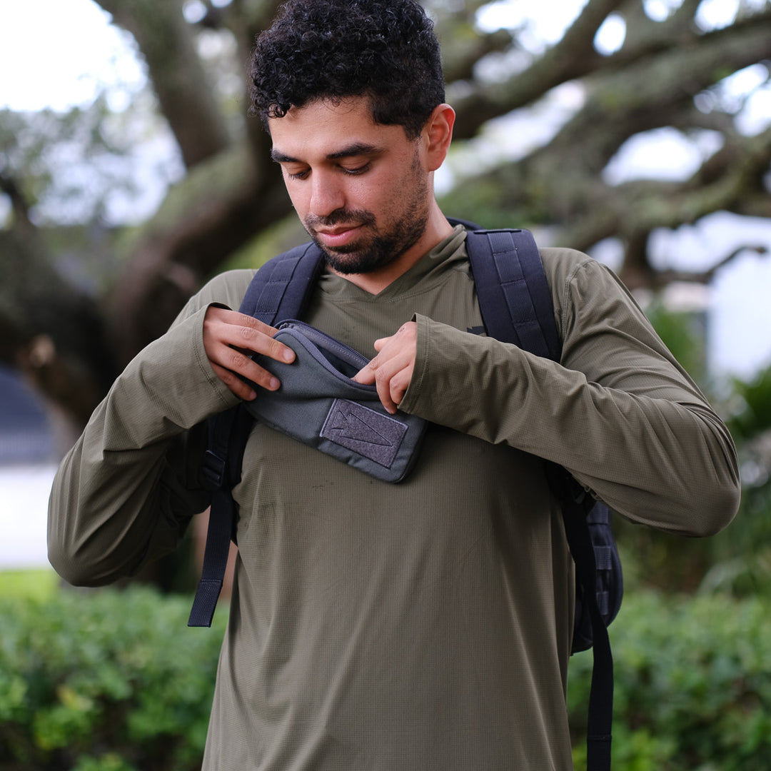 A man in a green shirt with a backpack puts a wallet into his GORUCK Sternum Pouch - Cordura outdoors.
