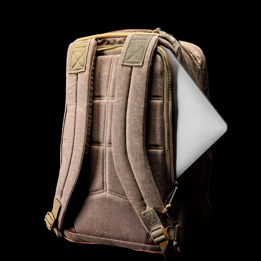 The GORUCK GR1 USA - Heritage backpack features padded straps and a laptop partially visible in the back pocket, displayed against a black background.