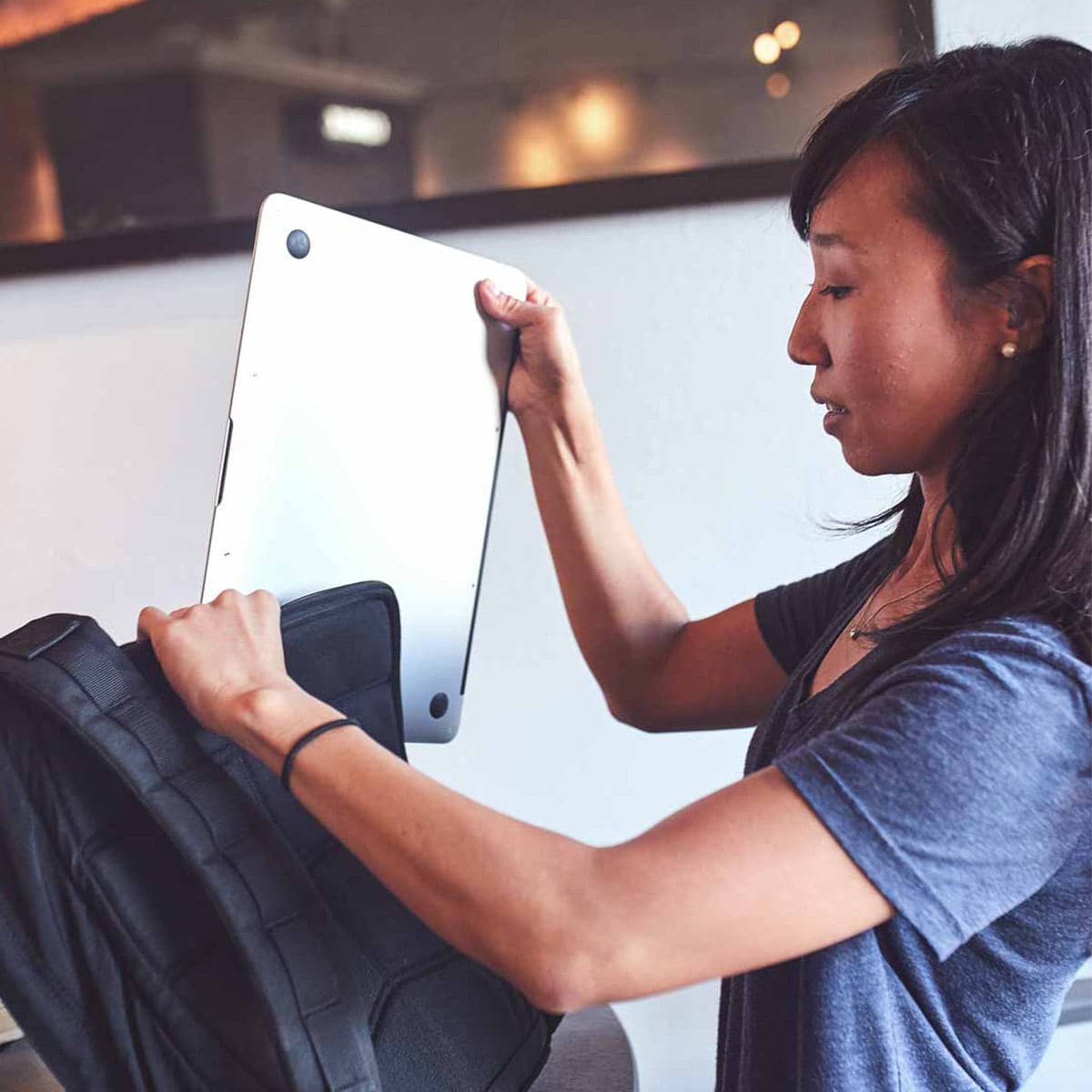 Woman placing laptop into GORUCK backpack, durable rucking gear for everyday carry.