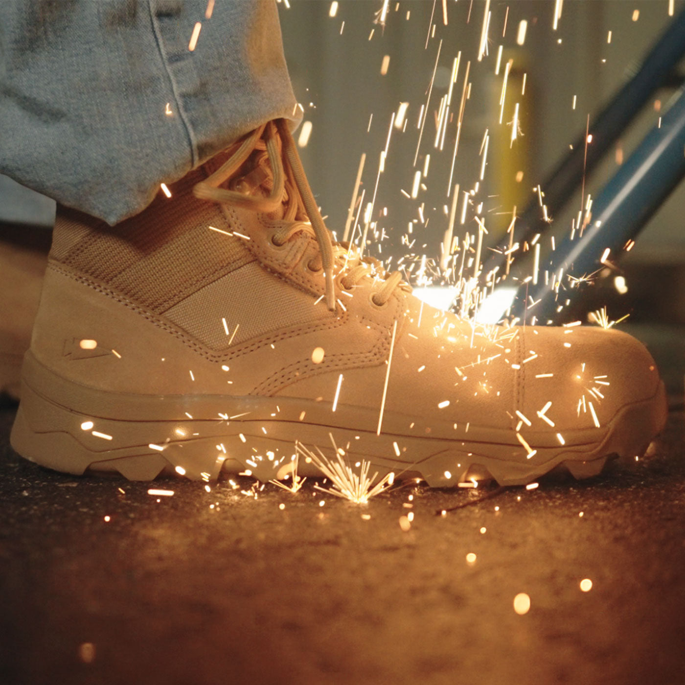 A tan work boot surrounded by flying sparks, with someone wearing light-colored pants.
