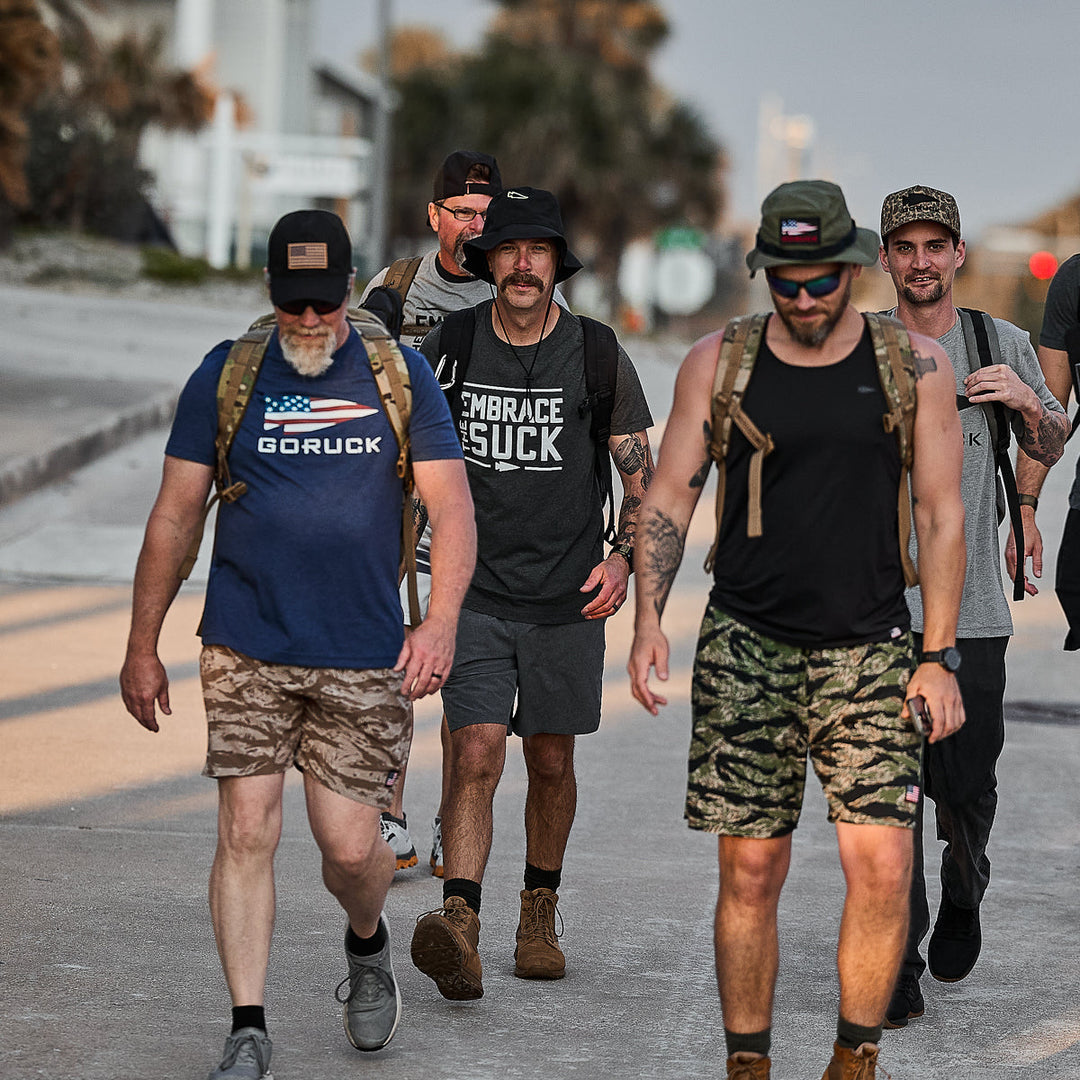 Five men in casual and athletic gear walk outdoors, embracing the challenge—a true nod to the USMC motto—while wearing the Embrace the Suck Tee - Tri-Blend by vendor-unknown.