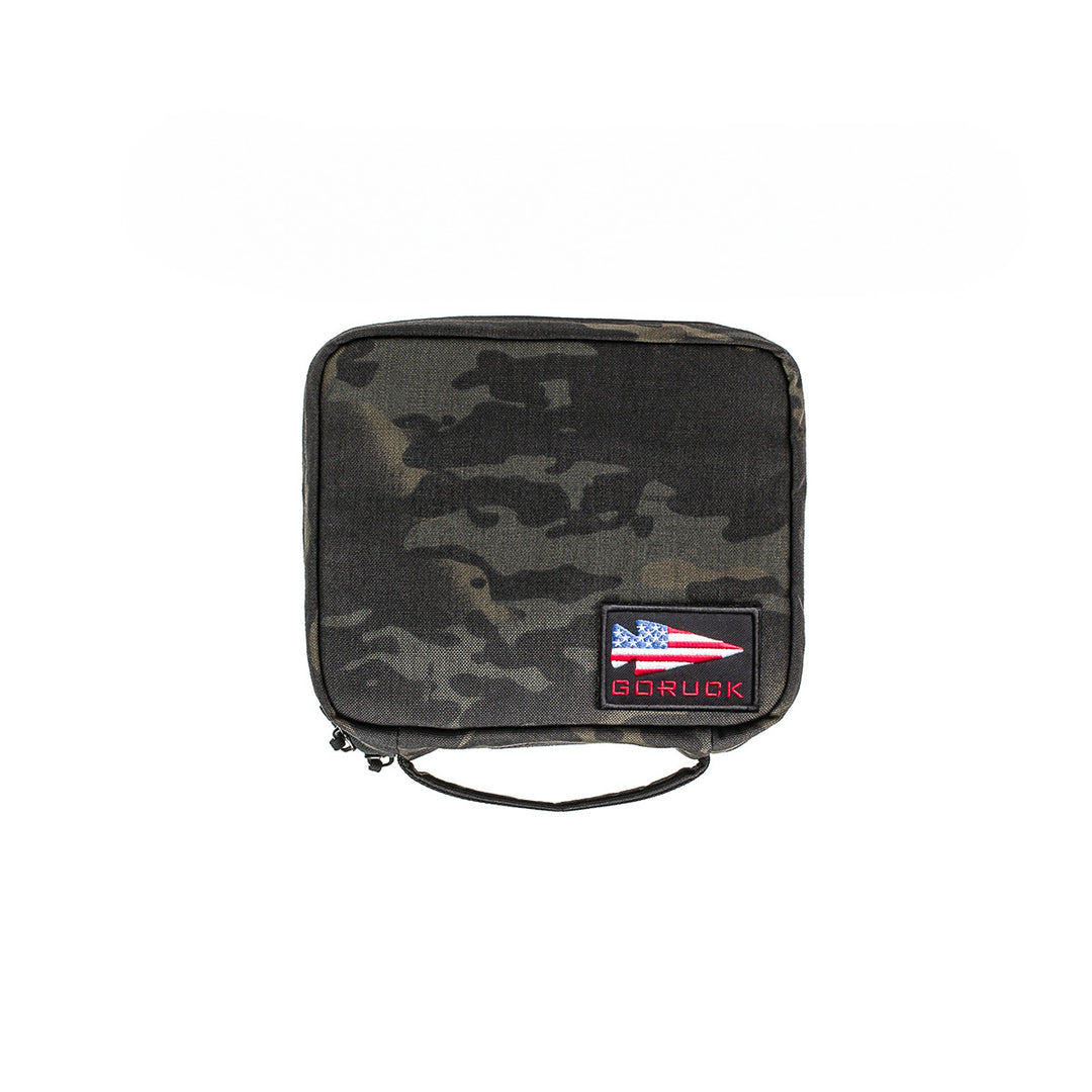 The GORUCK GR2 Field Pocket is a square camouflage pouch with a handle and American flag patch, made from 1000D Cordura. It features MOLLE webbing for easy attachment—ideal as an electronics organizer or everyday carry.