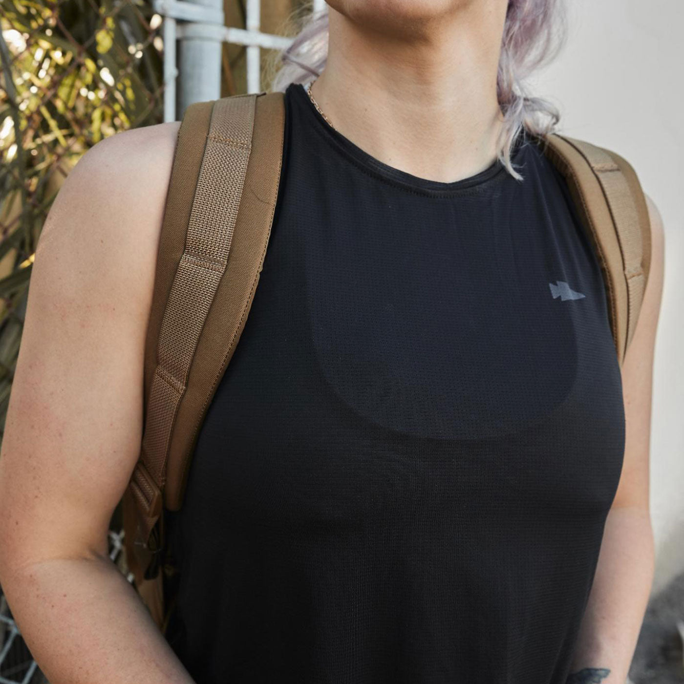 Person wearing a black sleeveless top and tan backpack straps, standing outdoors.
