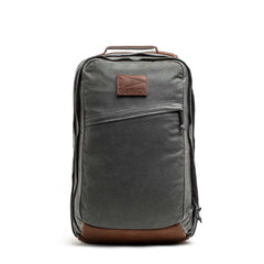The GORUCK GR2 - Heritage Waxed Canvas backpack features gray waxed canvas, brown Red Wing leather accents, a front zipper pocket, and a convenient top handle—an upright, stylish ruck perfect for travel.