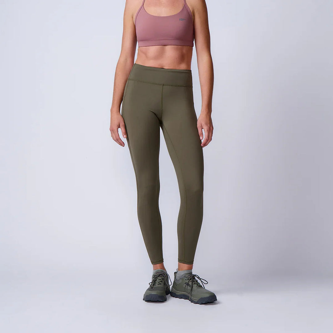 Woman wearing olive green GORUCK leggings, pink sports bra, rucking shoes in studio setting