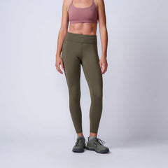 Woman wearing olive green GORUCK leggings, pink sports bra, rucking shoes in studio setting