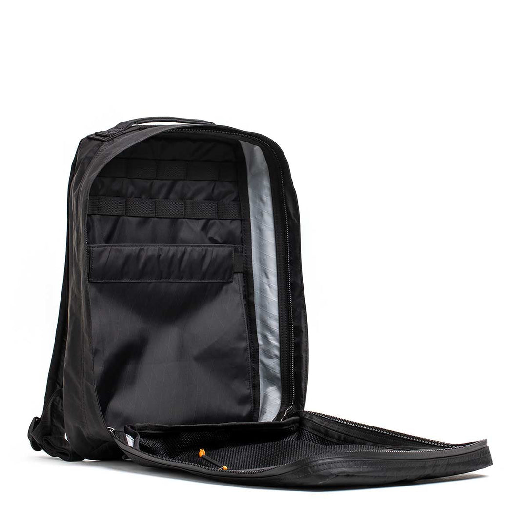 The GORUCK GR0 - X-PAC is a black, lightweight backpack, unzipped to reveal multiple inner compartments and storage pockets.