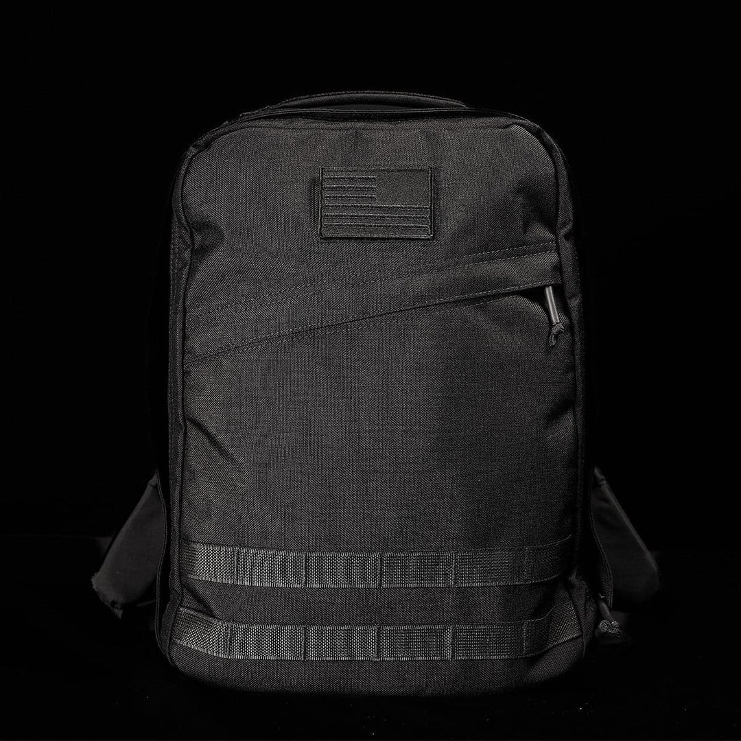 The GR0 - Cordura by GORUCK is a black tactical backpack set against a dark background. This compact backpack showcases a small patch on the top front, a diagonal zippered pocket, and horizontal straps at the bottom. Its bombproof laptop compartment enhances durability while maintaining a sleek, minimalist EDC design.