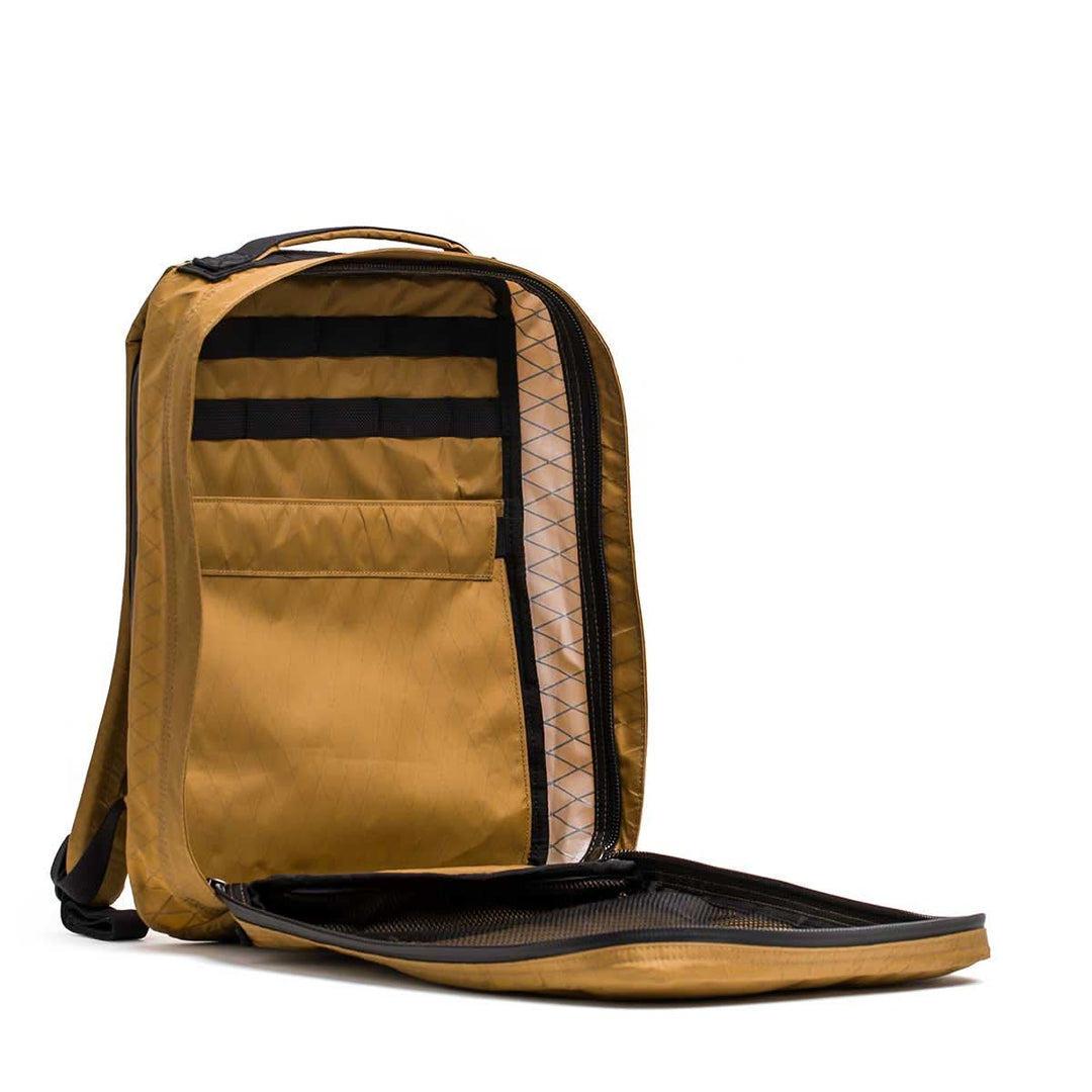 The GORUCK GR0 - X-PAC, a brown, lightweight backpack, is open to reveal its interior pockets and compartments against a white background.