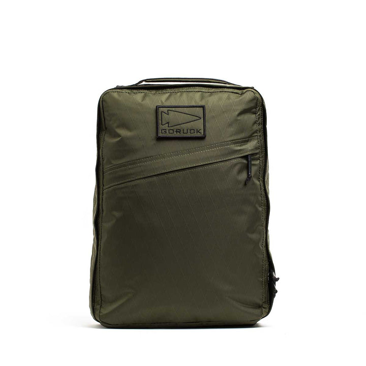 The GORUCK GR0 - X-PAC is an olive green, lightweight backpack with a front zipper pocket and a rectangular logo patch on the upper front, designed for everyday use.