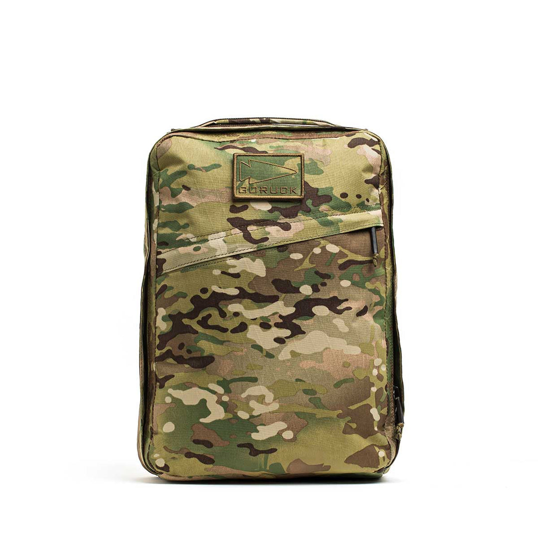 The GORUCK GR0 - X-PAC is a lightweight backpack in a camouflage pattern, shown upright with a top handle and front patch on a white background.